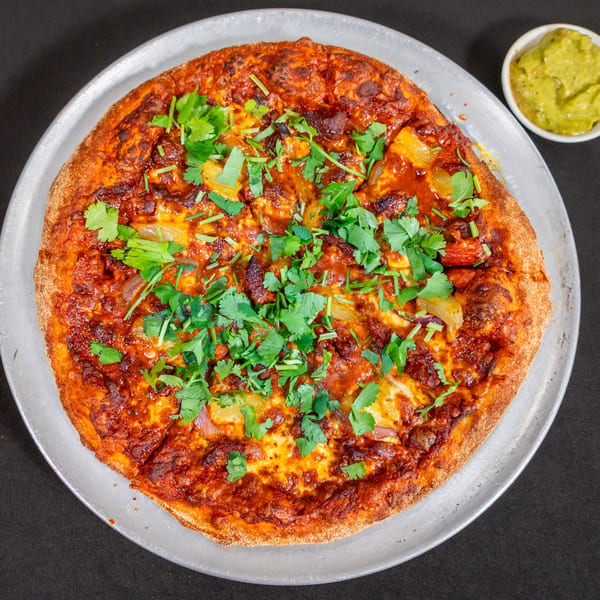 Soriano's Pizzeria pizza with red sauce, cheese, pineapple, and cilantro, with a side of guacamole.