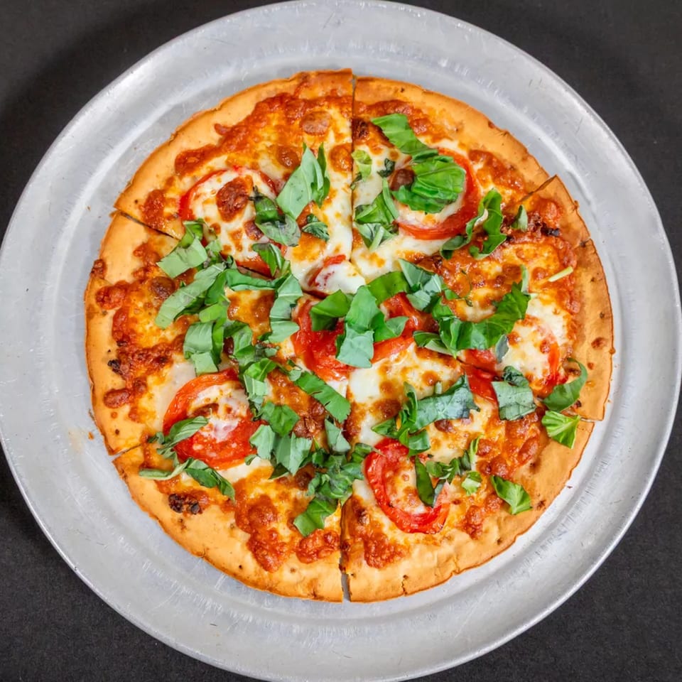 A Sorianos Pizzeria Margherita pizza with fresh basil and sliced tomatoes on a metal tray.