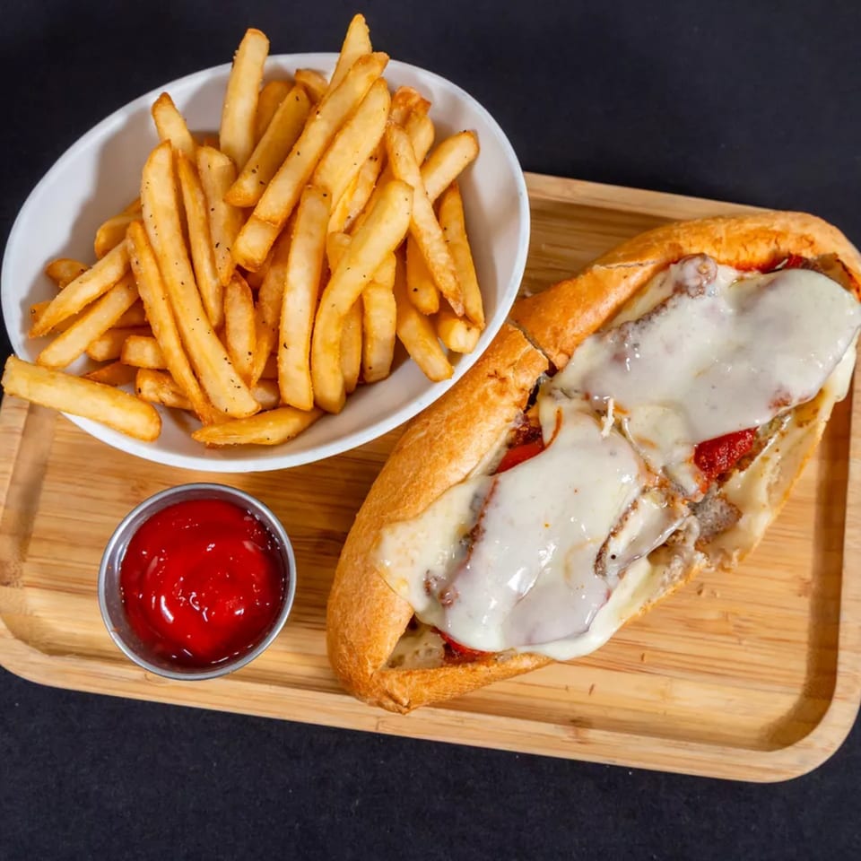 A Sorianos Pizzeria cheesesteak with melted cheese, a side of fries, and ketchup on a wooden tray.