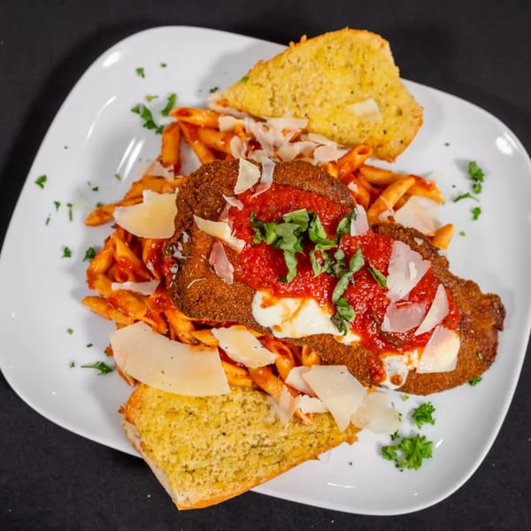 Chicken parmesan with penne pasta, tomato sauce, cheese, basil, and garlic bread on a white plate.
