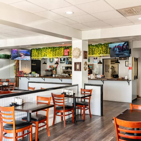 Interior of Sorianos Pizzeria with dining tables, chairs, a counter, and TVs showing sports.