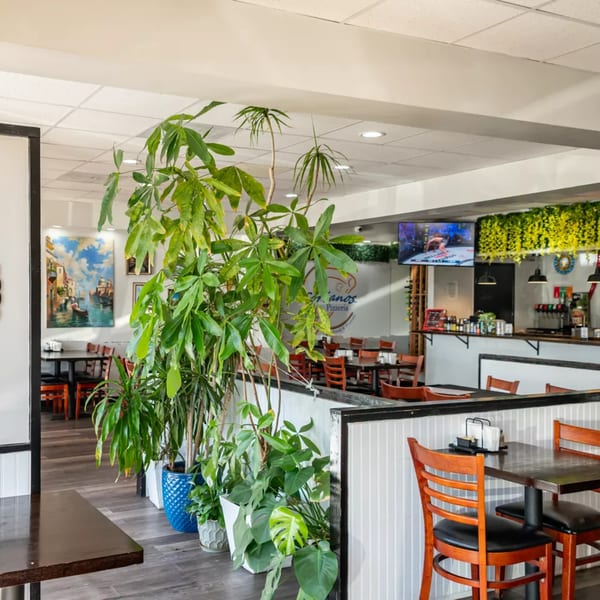 Interior of Sorianos Pizzeria with dining tables, chairs, potted plants, and a counter with drinks.