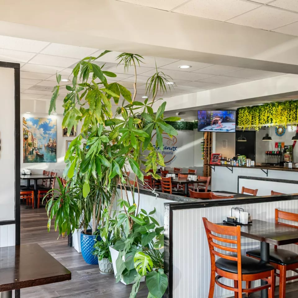 Interior of Sorianos Pizzeria with dining tables, chairs, potted plants, and a counter with drinks.