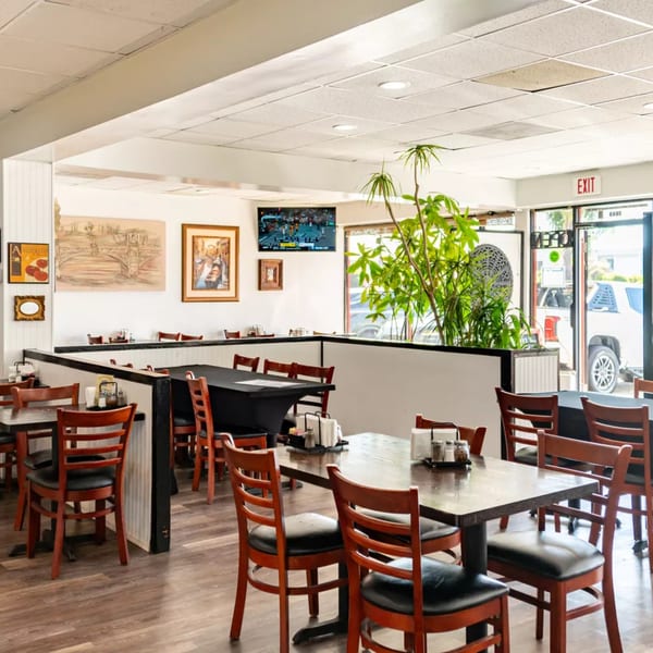 Interior of Sorianos Pizzeria with wooden tables and chairs, a TV, and plants, ready for diners.