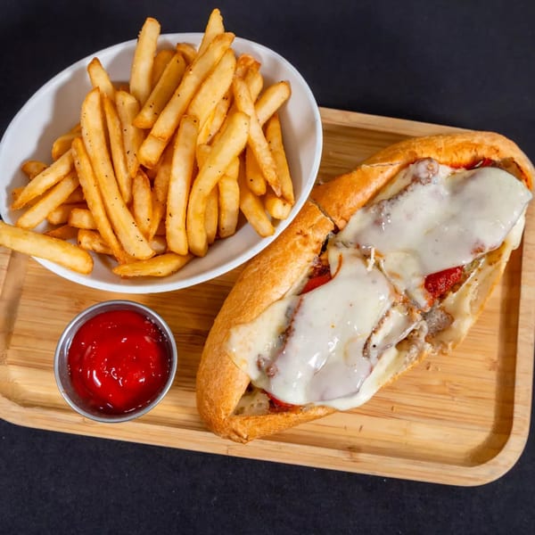 Cheesesteak sandwich with melted cheese, a side of golden fries, and ketchup on a wooden tray.