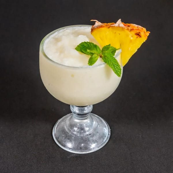 A frozen pineapple drink in a stemmed glass, garnished with a pineapple wedge and mint sprig.