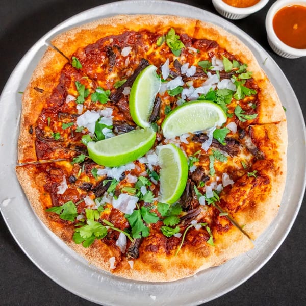 Sorianos Pizzeria's pizza with meat, cilantro, diced onions, and lime wedges on a metal tray.